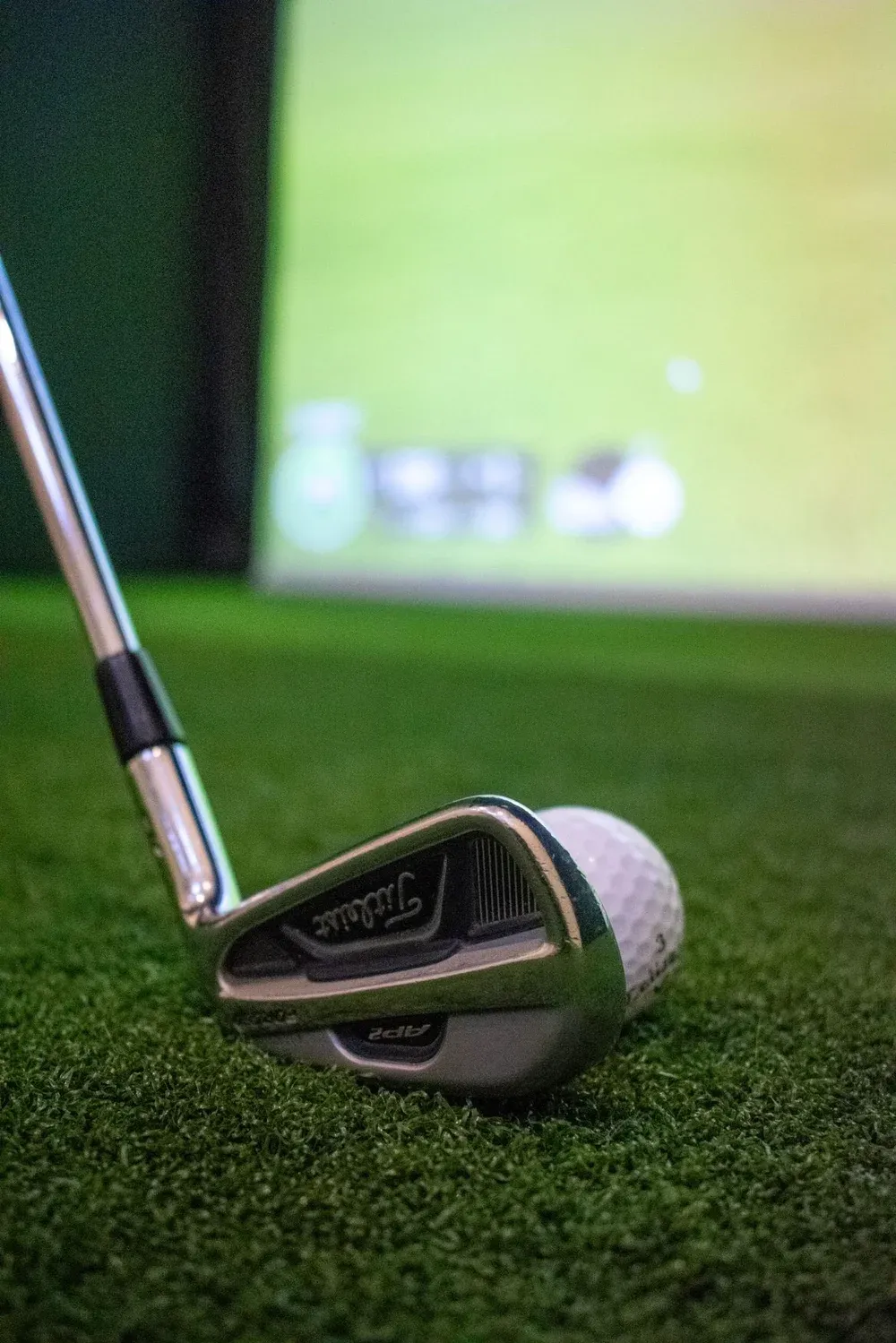 Close-up of an iron resting on the hitting mat in front of a Trackman screen