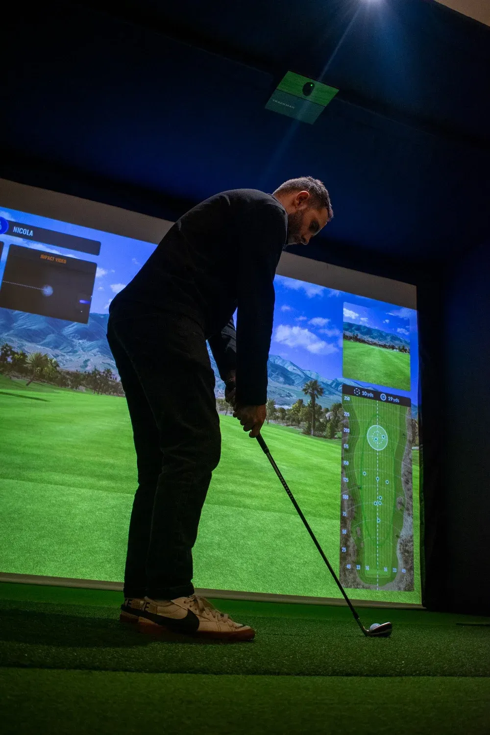 Golfer lining up a shot at a projected course in a simulator bay