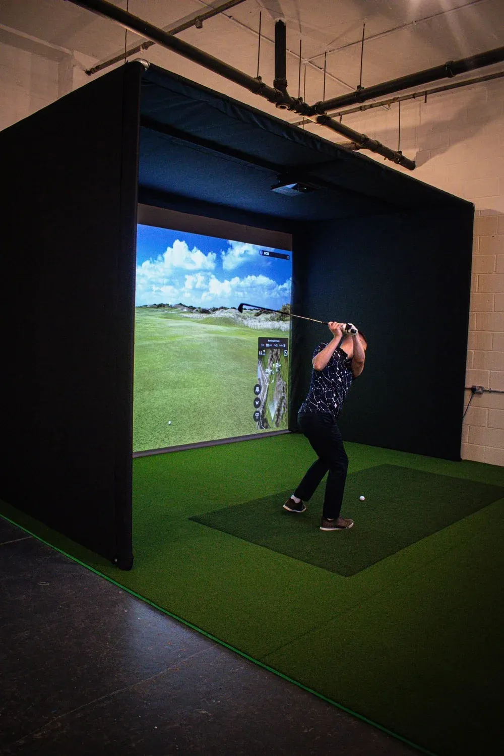 Member at the tee in a simulator bay with a course on the big screen
